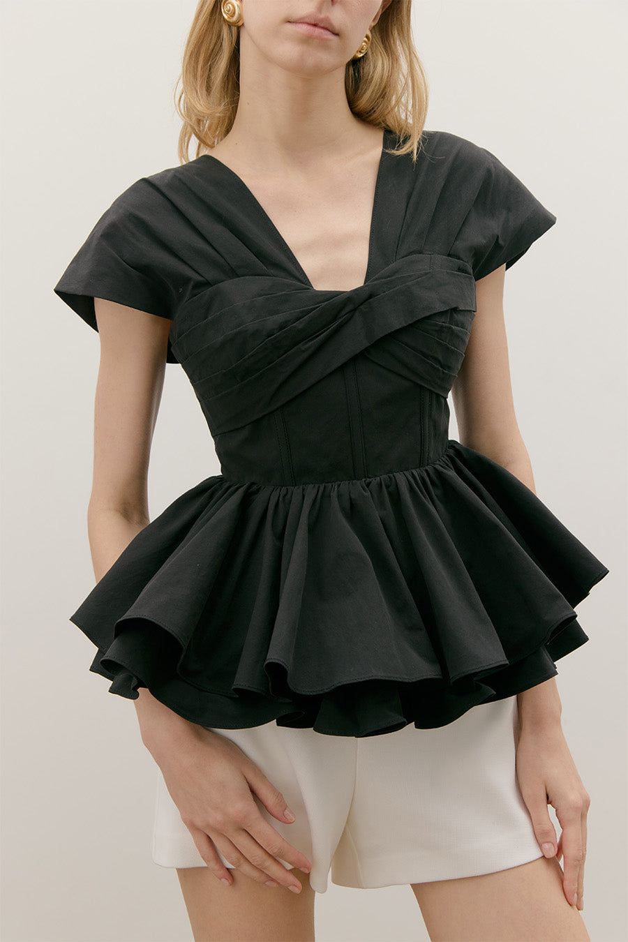 The crossover bodice creates a softly contoured shape, while the structured cap sleeves frame the shoulders with refined balance.