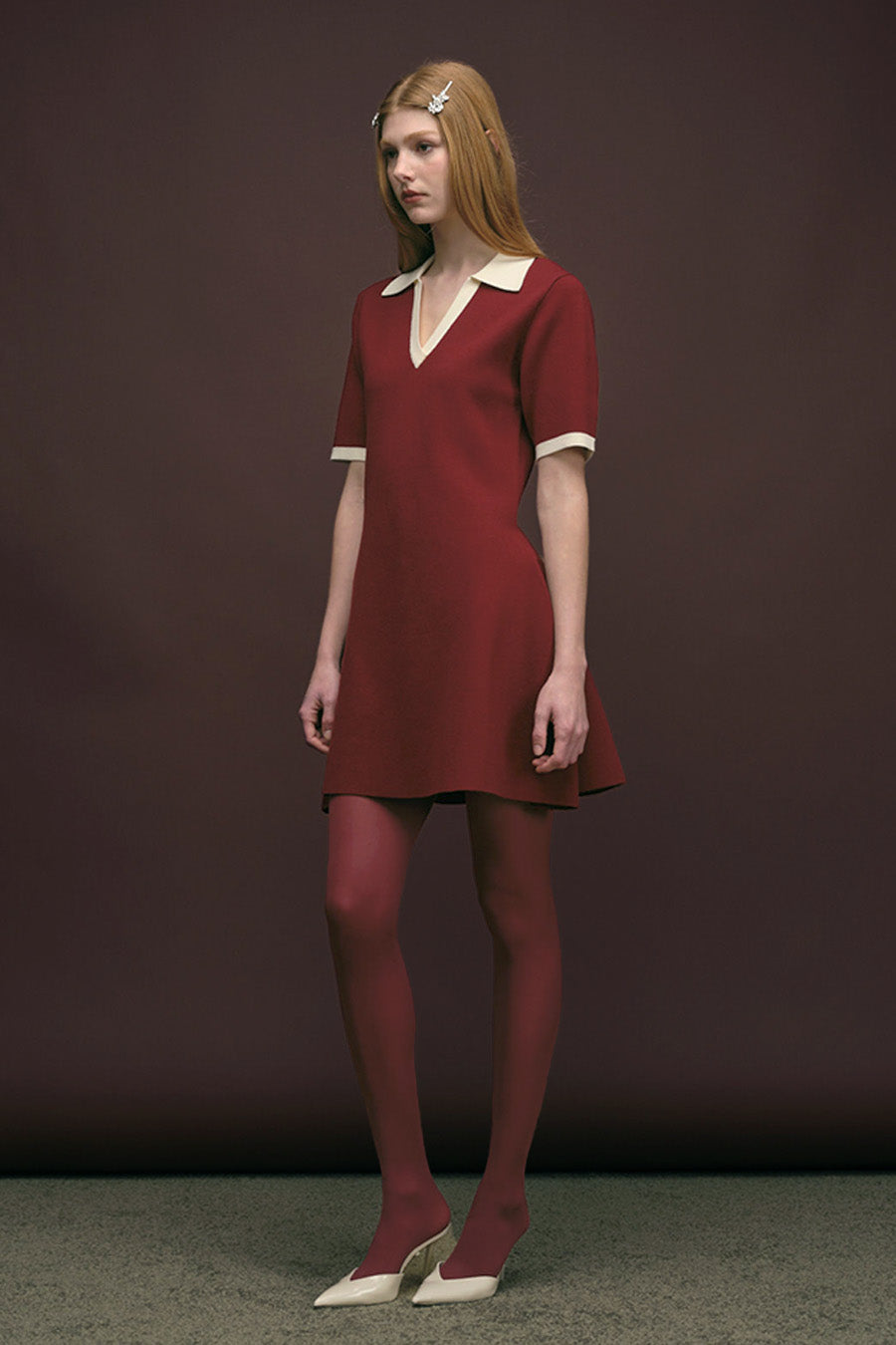 Featuring a soft V-neck framed by a contrasting ivory collar and matching cuffs, the silhouette is both modern and timeless.