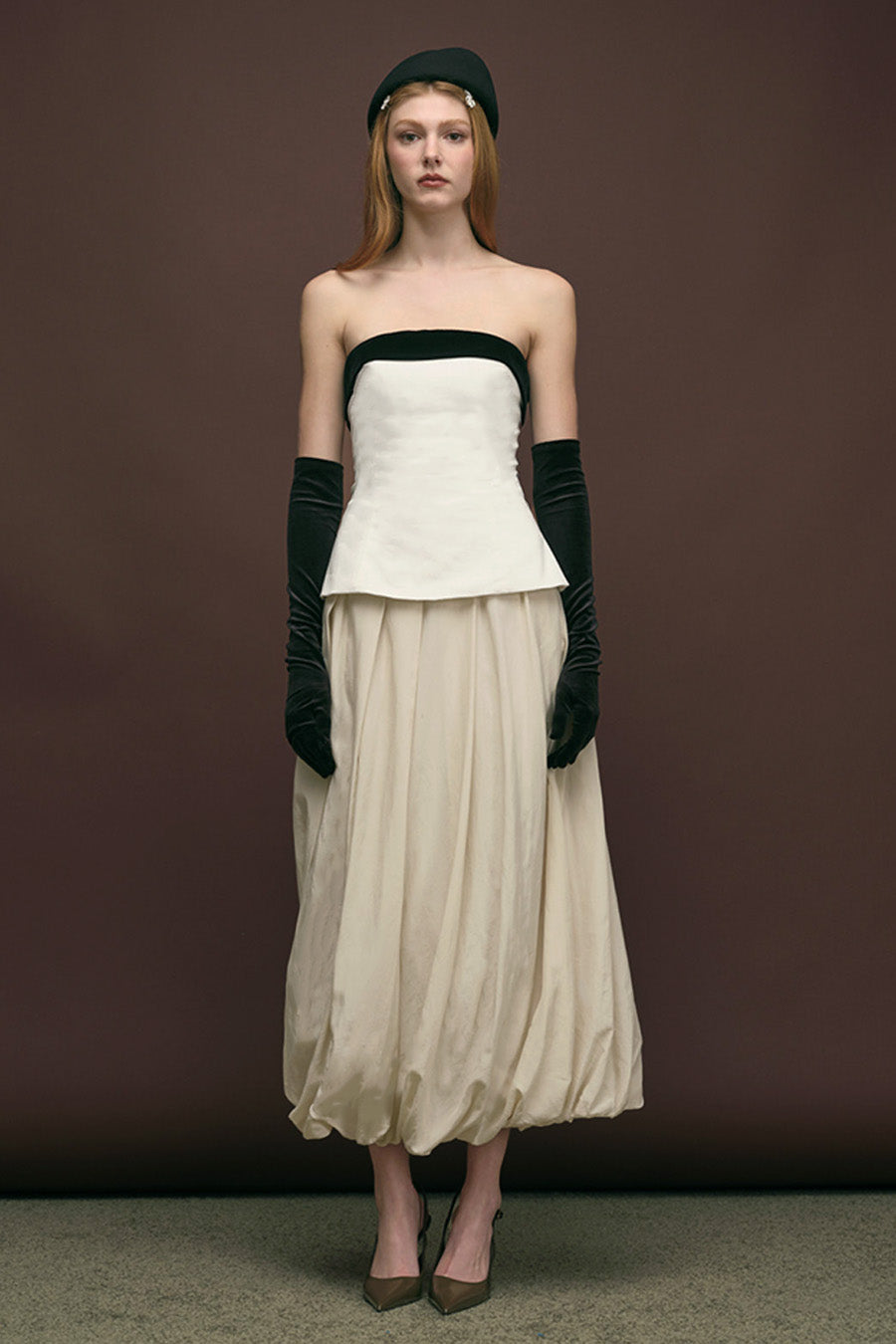 This sculptural strapless top is crafted in a refined ivory fabrication, defined by a bold contrasting black band that frames the neckline with graphic elegance.