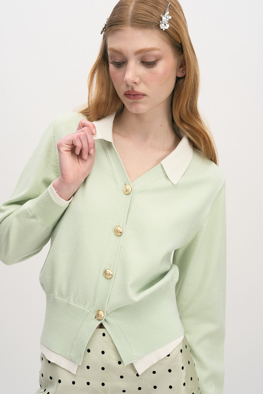 Designed with a gentle V-neck framed by a contrasting ivory collar, it features delicate gold-tone buttons that add a subtle touch of polish.