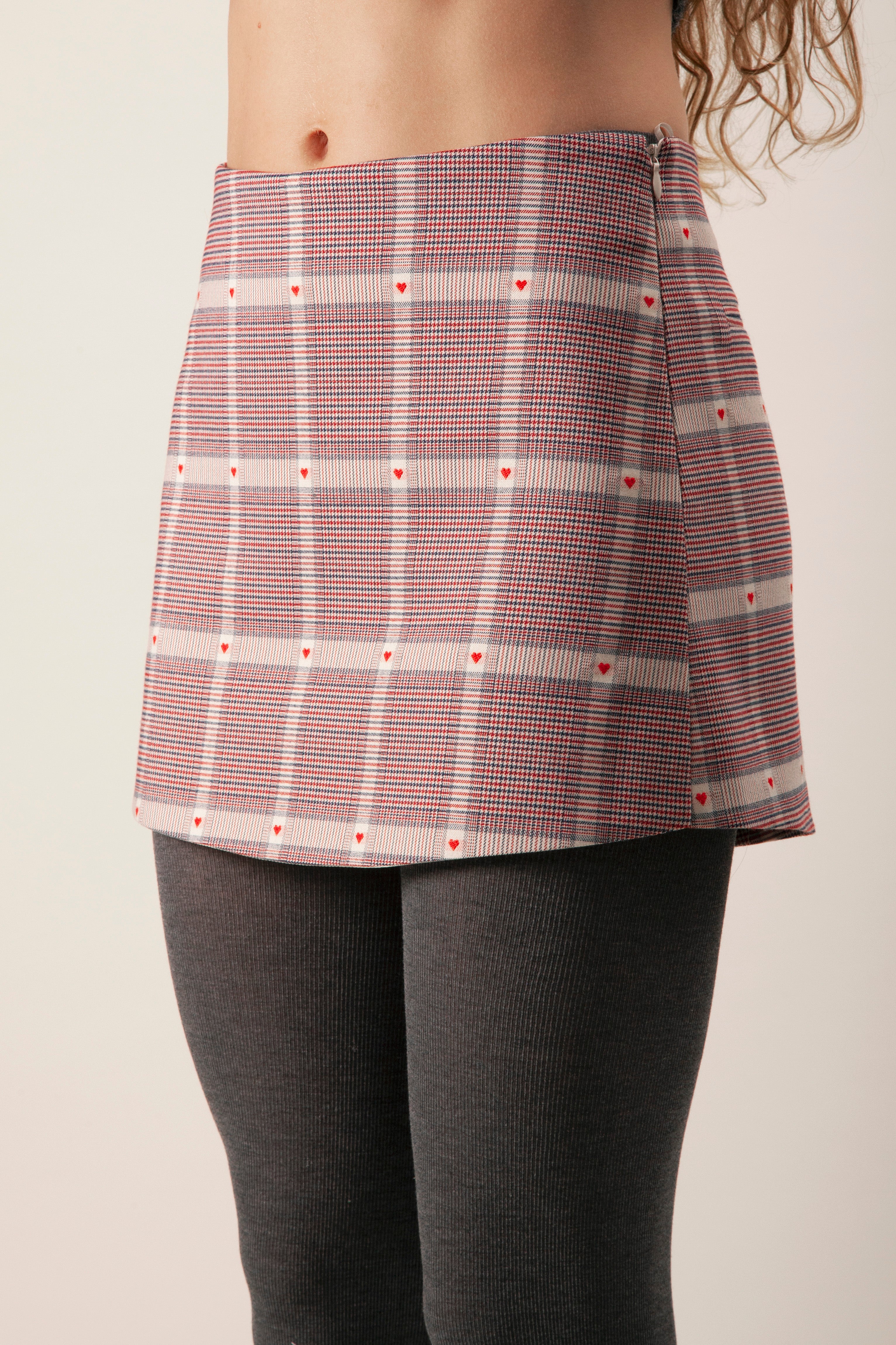 This tailored mini skirt is crafted in a finely woven plaid fabrication, distinguished by delicate heart motifs subtly integrated throughout the pattern.