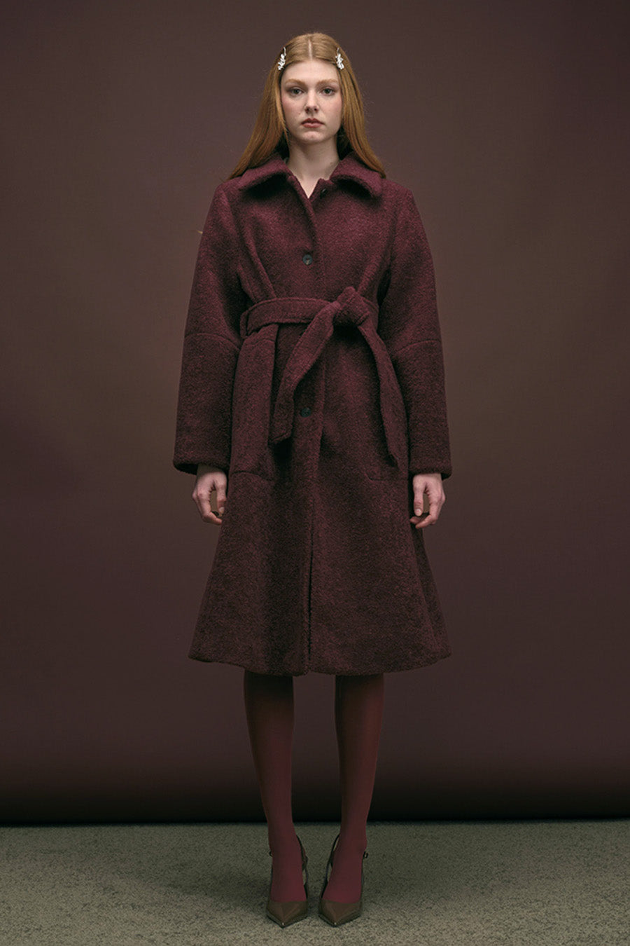 This elegant burgundy wool coat features a tailored longline silhouette with a matching self-tie belt for a flattering fit.