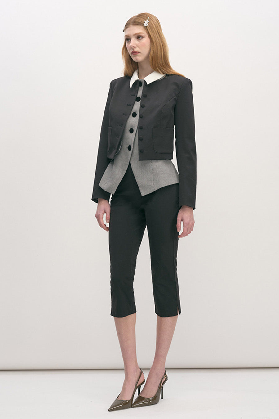 The design features sculptural covered buttons and clean flap pockets, while a contrasting layered under-panel adds depth and modern distinction.