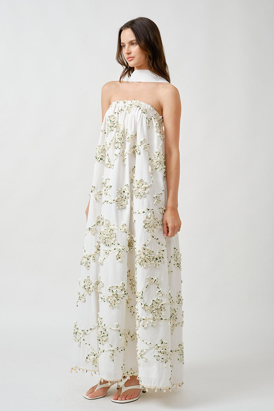 Featuring a refined halter neckline and softly gathered bodice, the dress drapes effortlessly over the body, creating graceful movement with every step.