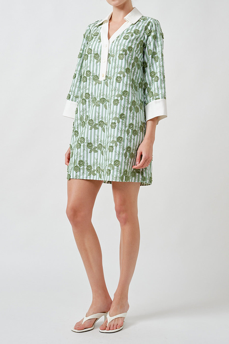 Crafted with a softly structured silhouette, it features a clean V-neckline framed by a crisp contrast collar and elegant three-quarter sleeves finished with turned-back cuffs.