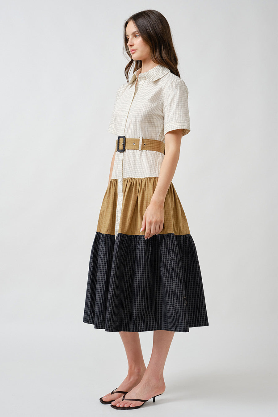 Crafted with a structured button-front bodice and crisp short sleeves, the silhouette is cinched at the waist with a statement belt that enhances definition while maintaining comfort.