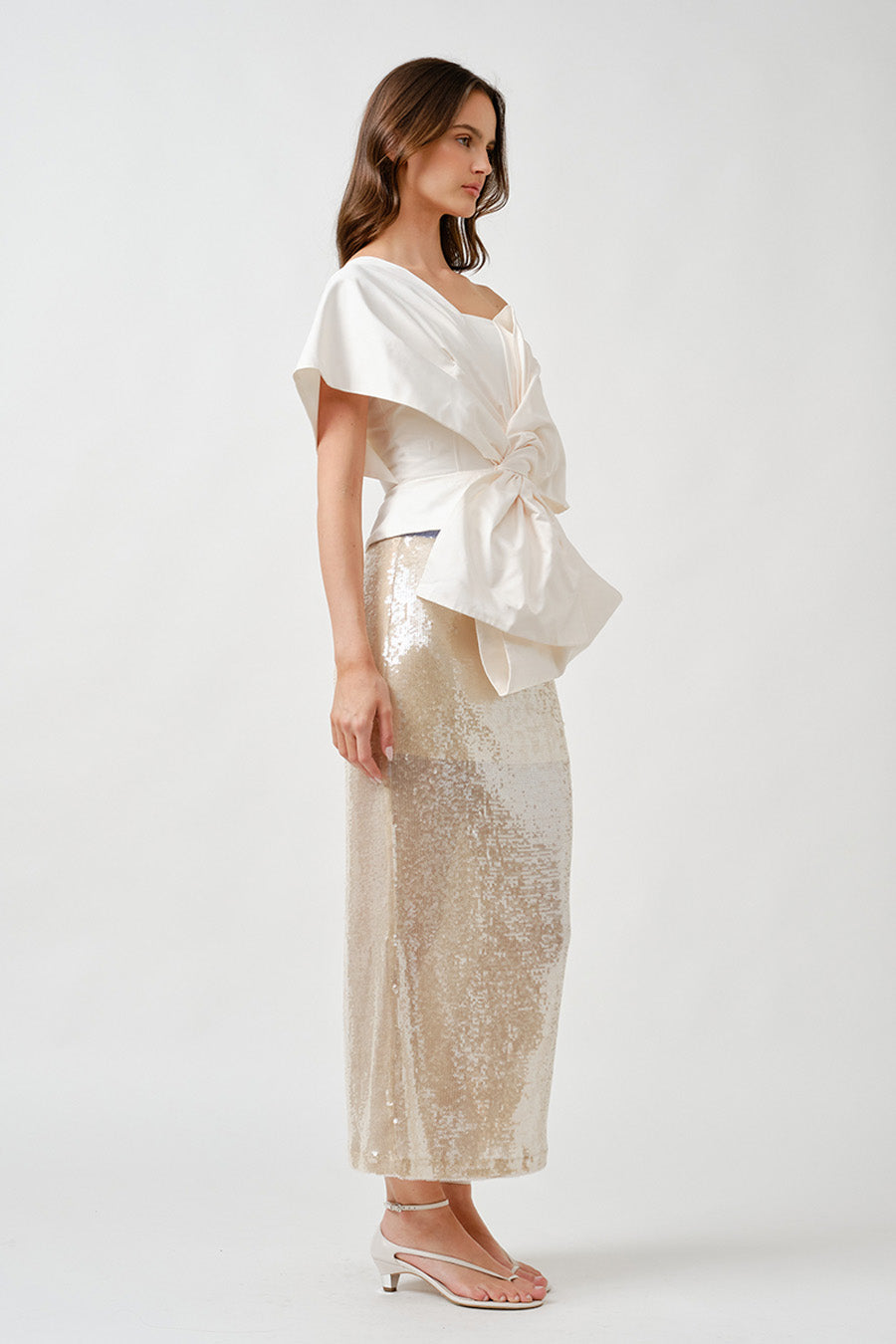 Crafted in a crisp ivory fabric, it features dramatic draping and a central knot detail that creates fluid volume and refined dimension.