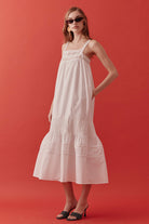 Designed with delicate lace detailing at the neckline and a softly flowing, tiered skirt, the silhouette evokes timeless romance with a modern sensibility.