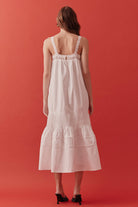 The relaxed bodice offers ease and movement, while subtle pleating and layered tiers add depth, texture, and graceful volume