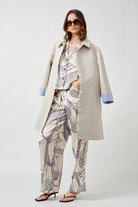 The classic collar and minimalist button closure create a timeless foundation, while subtle contrast lining at the cuffs introduces a discreet, contemporary detail.